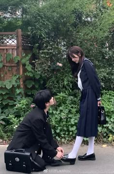 two people dressed in black and white are sitting on the ground, one is holding a briefcase