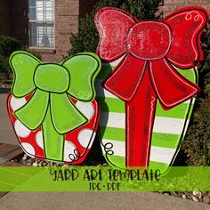 two large green and red christmas presents on display in front of a brick building with the words yard art temple