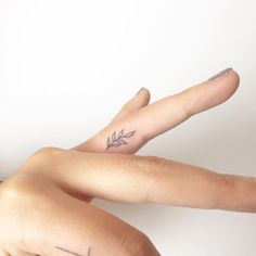 two fingers with small tattoos on them, one is pointing at the camera and the other has