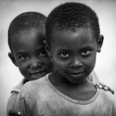 two young boys standing next to each other in front of a white background with one boy looking at the camera