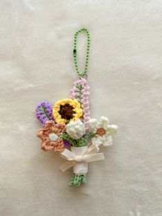 a crocheted flower bouquet hanging on a white blanket with a green string attached to it