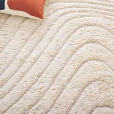 a white rug with wavy lines and a red pillow on the floor next to it