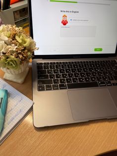 an open laptop computer sitting on top of a wooden desk next to a flower vase