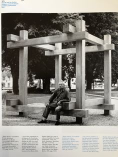 a man sitting on top of a bench in front of a wooden structure with columns