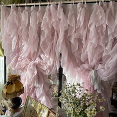 pink ruffled curtains hanging from a window with pictures and flowers in the foreground