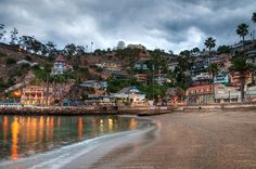 a beach with houses on the hill in the background and water coming up from the shore