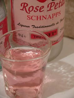 a glass filled with pink liquid sitting on top of a counter next to a bottle