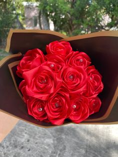 a bouquet of red roses is held in a brown paper box with jewels on it