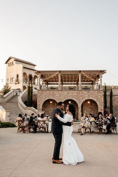 a bride and groom dance in front of an outdoor venue