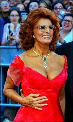 an older woman in a red dress with her hands on her hips smiling at the camera