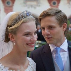 a man in a suit and tie standing next to a woman wearing a tiara