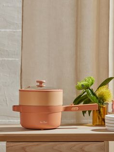 a pink pot sitting on top of a wooden table next to a vase with flowers