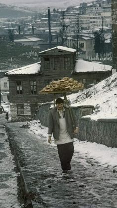 a man walking down a snow covered road carrying an umbrella on top of his head