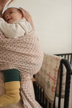 a woman holding a baby wrapped in a wrap on top of a crib next to a wall