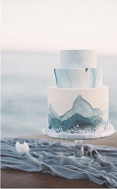 a three tiered cake sitting on top of a wooden table next to the ocean