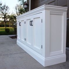 a white cabinet sitting on the side of a driveway next to a garage door and grass