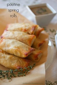 three spring rolls on a plate with dipping sauce in the middle and herbs sprinkled around them