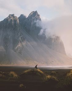 a man standing on top of a grass covered field next to a large mountain range