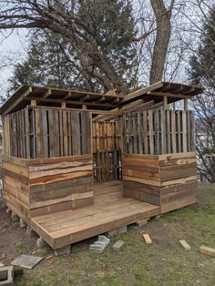 a small wooden structure sitting on top of a grass covered field next to a tree