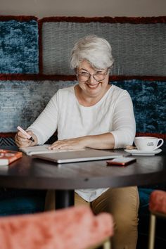 an older woman sitting at a table with a notebook and pen in her hand, smiling