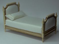 a miniature bed with white sheets and pillows on it's sides, against a plain background