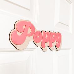 a wooden sign that says poppy hanging on a door handle with the word poppy painted in pink