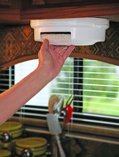 a person is holding up a white air conditioner in front of a kitchen window