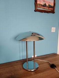 a table lamp sitting on top of a wooden floor next to a wall with a painting hanging above it