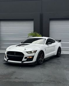 a white mustang parked in front of two garage doors