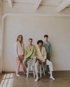 four men sitting on stools in front of a white wall