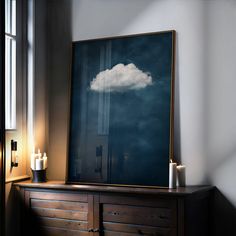 a wooden dresser topped with a painting and two candles on top of it next to a window