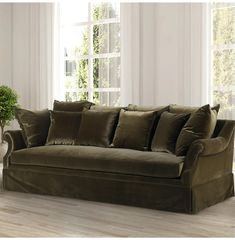 a couch with pillows on it in front of a white wall and window, next to a potted plant