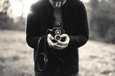 black and white photograph of a man holding an old camera in his hands while looking at it