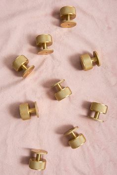 there are many small gold cufflinks on the pink blanketed tablecloth,