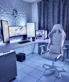 a chair sitting in front of two computer monitors on top of a white desk next to a blue curtain