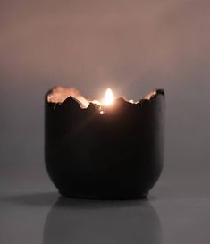 a lit candle sitting on top of a table next to a black bowl filled with water