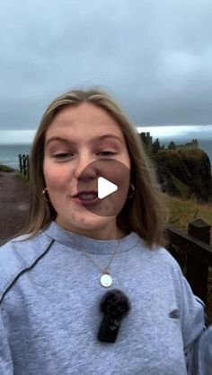 a woman making a funny face while standing in front of the ocean on a cloudy day