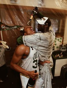 two basketball players hug each other in the locker room while one holds his head on another player's shoulders