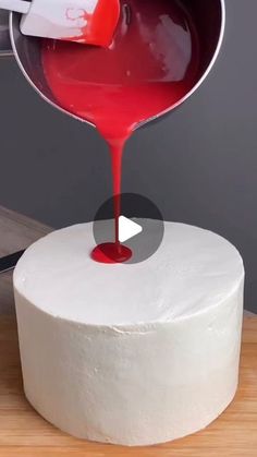 someone pouring red liquid on top of a white cake