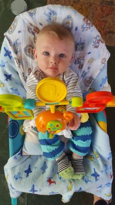 a baby sitting in a highchair with toys on it's back legs