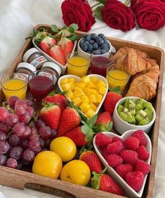 a wooden tray filled with fruit and veggies next to croissants