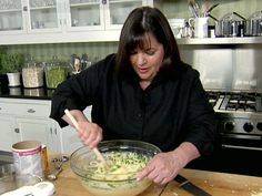 a woman mixing food in a bowl on top of a wooden table with utensils