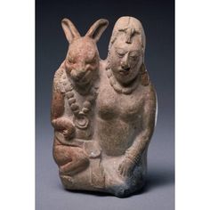 an ancient statue of a woman and a rabbit holding a baby in her lap, with one hand on the ground