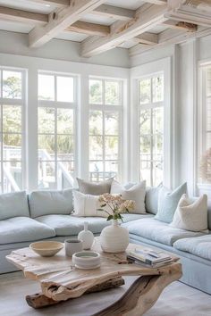 a living room filled with white furniture and lots of window sill space next to a large wooden coffee table