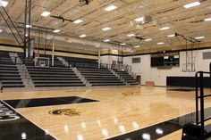 an empty basketball court in a gym with lights on the ceiling and bleachers