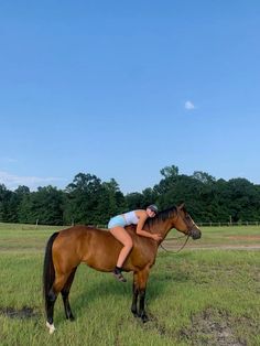 a woman riding on the back of a brown horse in a green field with trees