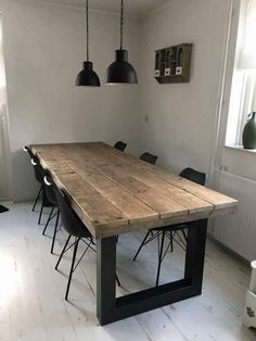 a wooden table with black chairs in a white walled dining room, surrounded by hanging lights