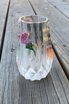 a glass vase with flowers painted on it sitting on a wooden table outside in the sun