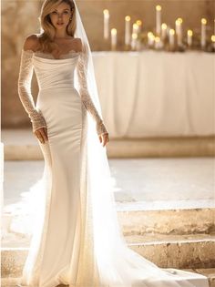 a woman in a wedding dress standing on stairs with her arms around her waist and wearing a veil