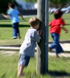 two young boys playing on a wooden pole in the park while another boy runs behind them